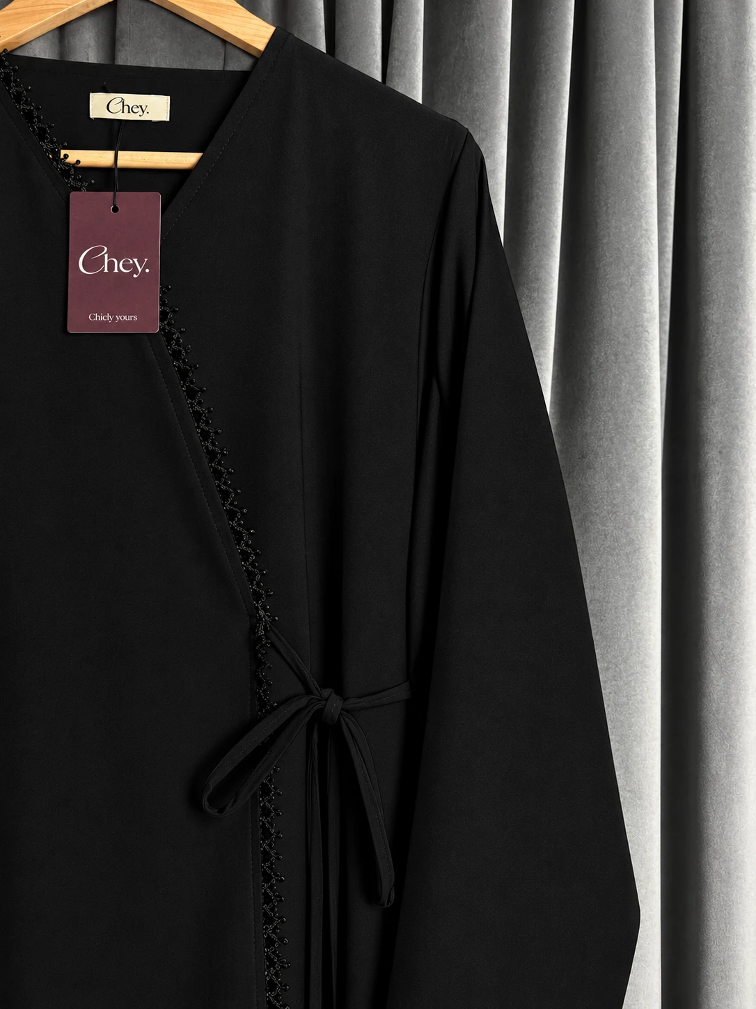 Black Chey. wrap abaya with a side tie and lace edge, on a hanger with the Chey. label and tag
